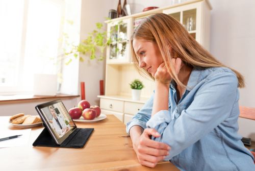 Woman sitting at a table doing a telehealth video with her doctor