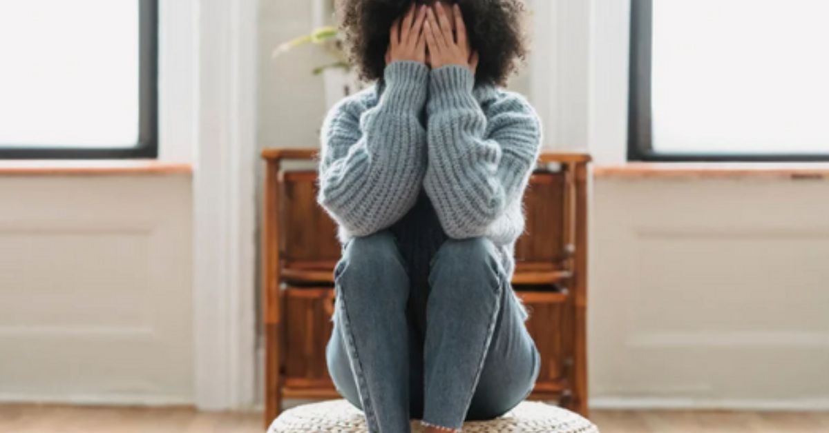 A woman sitting and covering her face with her hands.