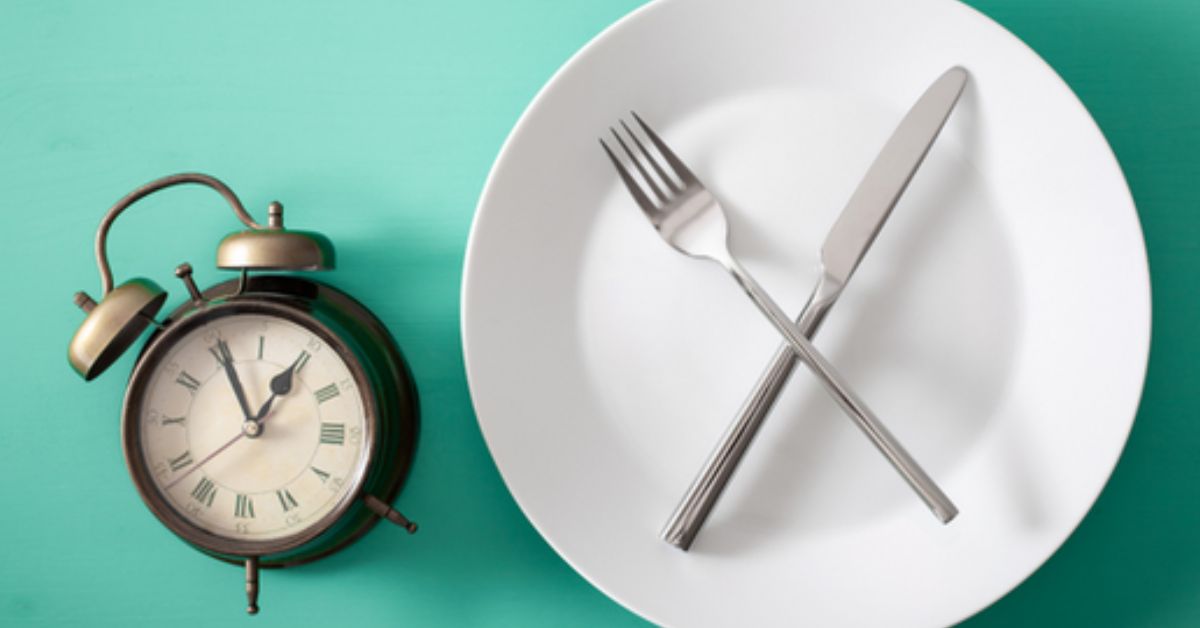 Plate with silverware crossed on top and a clock next to it